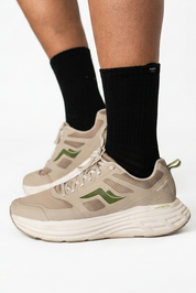 A person wearing beige and olive green athletic sneakers with black Pumpt Apparel crew socks.