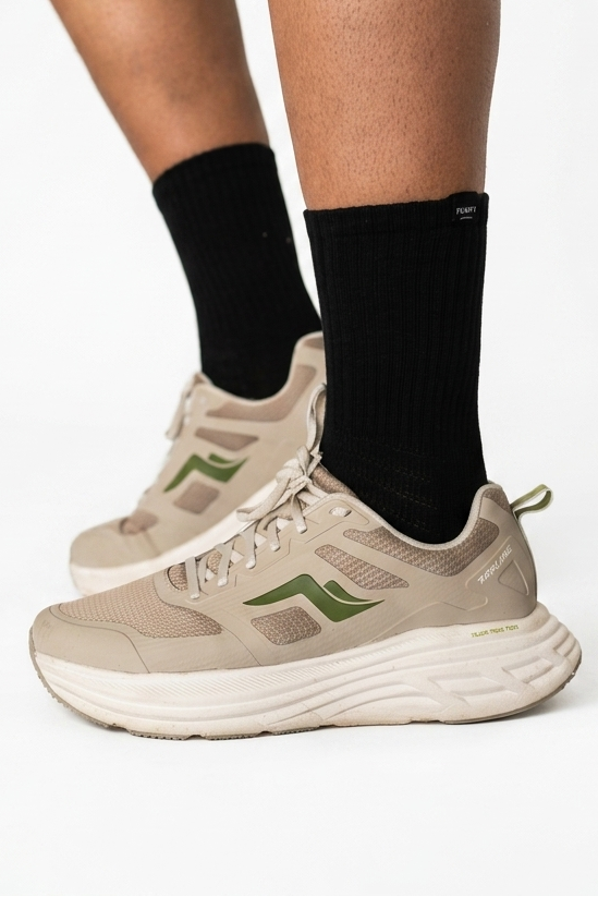 A person wearing beige and olive green athletic sneakers with black Pumpt Apparel crew socks.