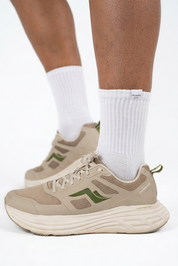 Beige athletic sneakers with green accents worn with white crew socks, shown on a model's feet against a white studio background.